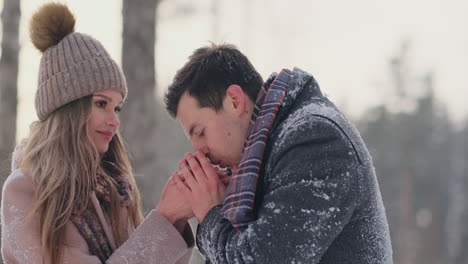 A-couple-in-love-a-man-warms-his-hands-with-his-breath-a-woman.-Stylish-couple-in-the-Park-in-winter-for-a-walk.